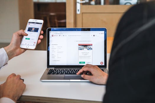 Hands using smartphone and laptop for digital browsing in an office setting, showcasing remote work culture.